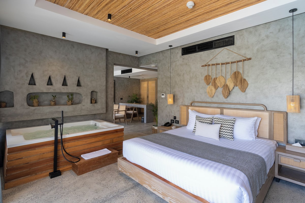 Une chambre d’hôtel moderne avec un grand lit, un banc en bois, une baignoire et un espace bureau.