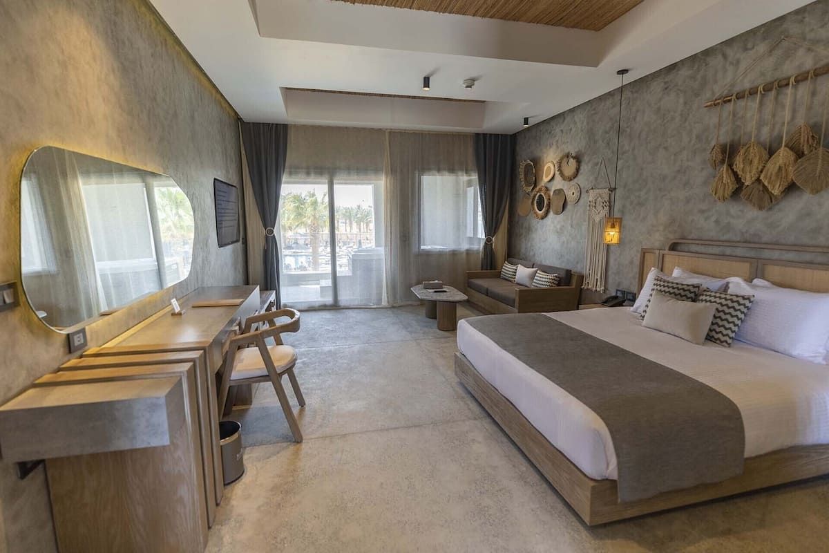 Une chambre d’hôtel moderne, dotée d’un grand lit, d’un bureau avec une chaise, d’une petite table et d’un grand miroir.