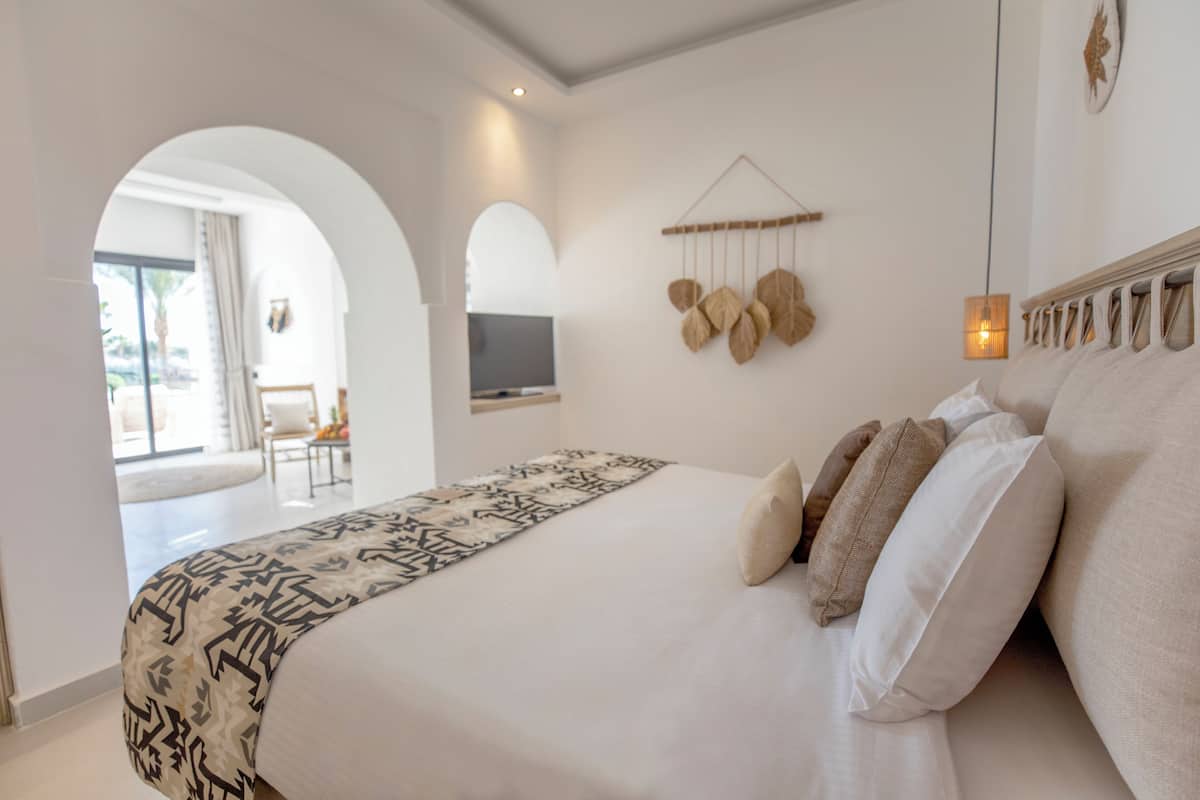 Une chambre avec un grand lit, un téléviseur fixé au mur et une vue sur l’extérieur par une porte en arc de cercle.