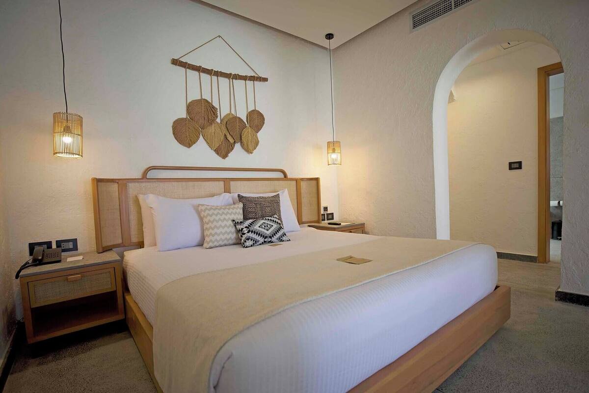 Une chambre d’hôtel avec un grand lit, deux tables de chevet, un luminaire fixé au mur et un chambranle en arc de cercle.