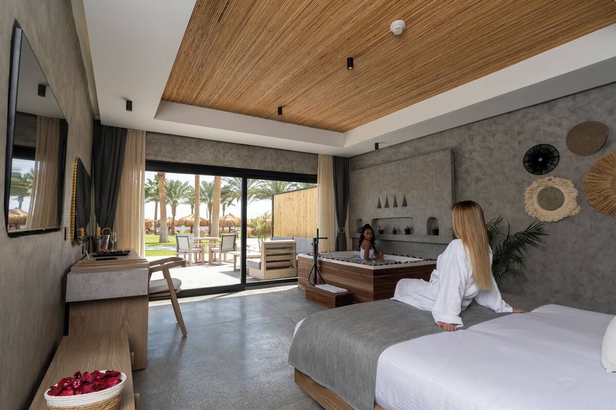 Une chambre d’hôtel moderne dotée d’un grand lit, d’un coin salon avec un bureau et offrant une vue sur l’extérieur.