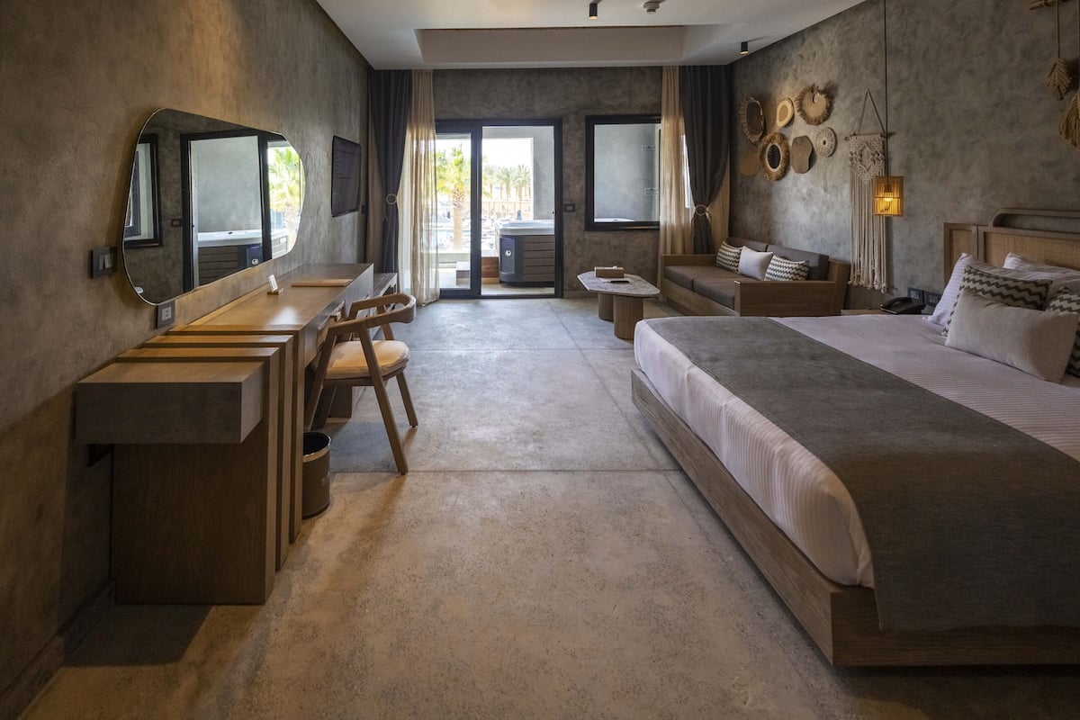 Une chambre d’hôtel moderne avec un grand lit, un bureau avec une chaise, une petite table et un grand miroir.