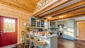 A wooden interior with a red door, a kitchen with light blue cabinets, and a breakfast bar with chairs. - Custom Craftsman Chalet🏡Fenced Yard for Pets🍃Aspens, Hot Tub 💰$0 Cleaning & Pet Fee (Fairplay)