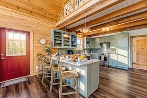 A wooden interior with a red door, a kitchen with light blue cabinets, and a breakfast bar with chairs. - Custom Craftsman Chalet🏡Fenced Yard for Pets🍃Aspens, Hot Tub 💰$0 Cleaning & Pet Fee (Fairplay)