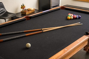 Une table de billard avec des queues, des billes et un petit arrangement floral.