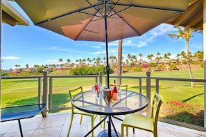 Un patio con una mesa, sillas, una sombrilla grande y vistas a un campo de golf y casas al fondo.
