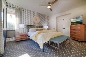 Ein Schlafzimmer mit einem Bett, Nachttischen, einer Kommode, einem Deckenventilator und einem großen Fenster mit Vorhängen.