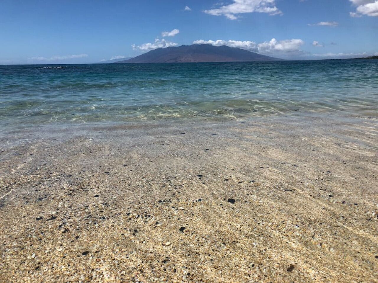 Une plage dégagée, avec des galets bien visibles, et une montagne qui se profile à l’horizon.
