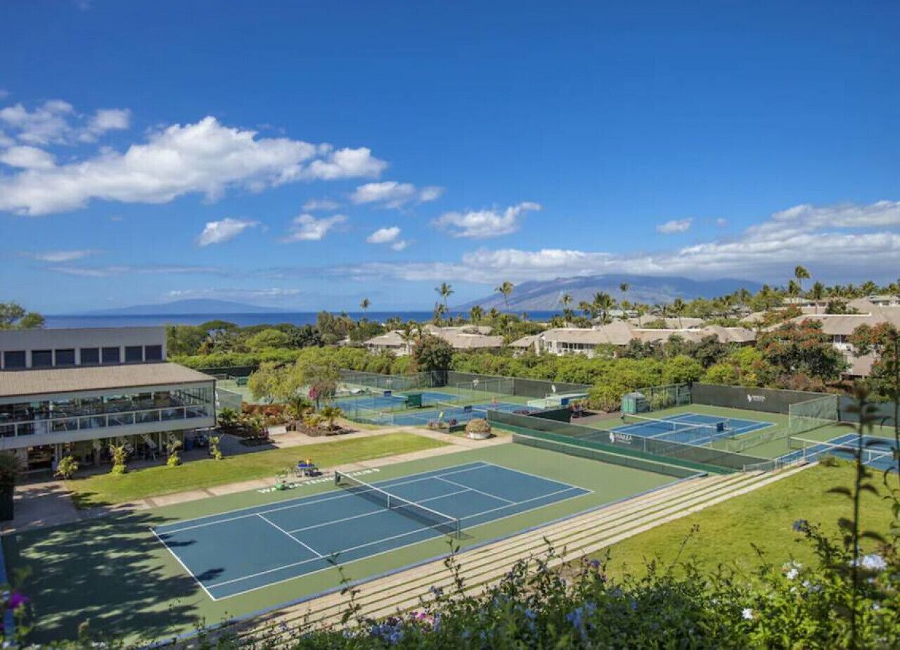 Ein Tennisplatzkomplex mit mehreren Plätzen, umgeben von Grünflächen und Gebäuden.