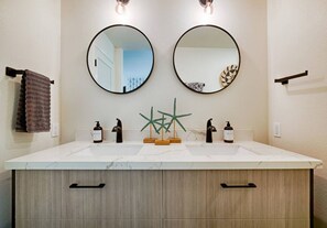 Un baño con dos espejos redondos, un lavabo blanco y un armario de madera con dos cajones.