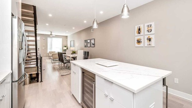 Una cucina moderna con piano di lavoro in marmo bianco, elettrodomestici in acciaio inossidabile e lampade a sospensione.