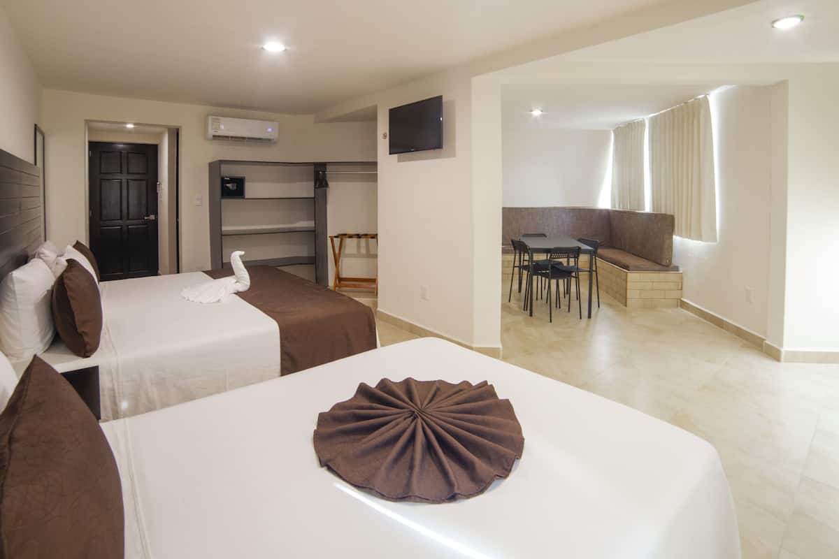 Une chambre d’hôtel avec deux lits, une télévision, un coin repas avec une table et des chaises, et une fenêtre avec des rideaux.
