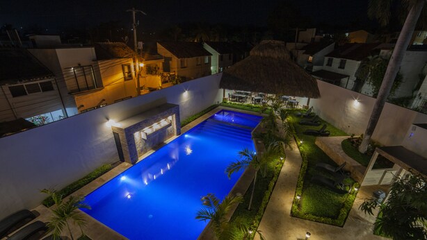 A nighttime view of a resort with a swimming pool, lounge chairs, and a thatched-roof structure. - Mayev Express (Santa María Huatulco)