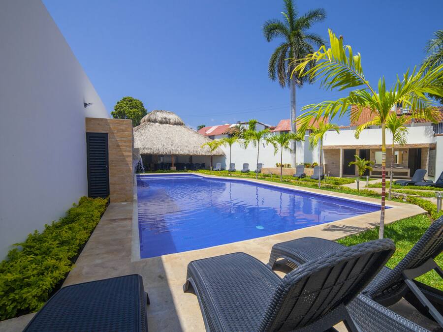 A swimming pool with lounge chairs, a thatched-roof structure, and palm trees.