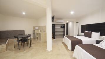 Quarto de hotel com duas camas, uma mesa de trabalho com cadeira, cozinha compacta e área de estar.