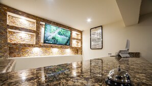 A reception area with a granite counter, a television mounted on a brick wall, and a framed menu on the wall. - Mayev Express (Santa María Huatulco)