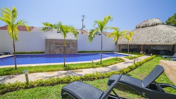 A swimming pool with a stone wall, palm trees, and lounge chairs in a garden setting.