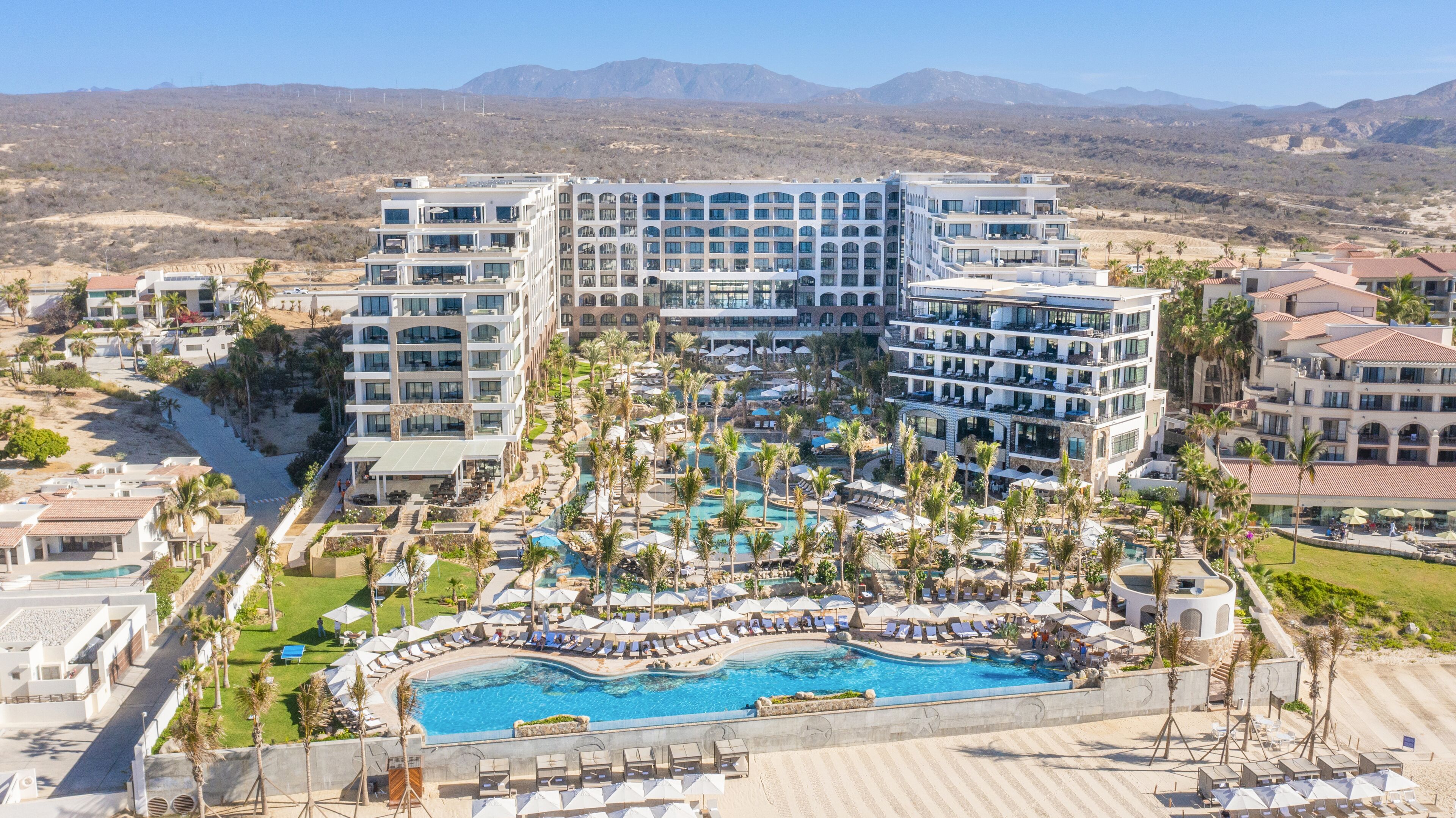 A resort with multiple buildings, a central swimming pool, and palm trees.