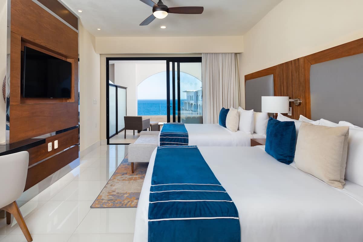 Ein Hotelzimmer mit zwei Betten, einem Fernseher, einem Deckenventilator und Meerblick.