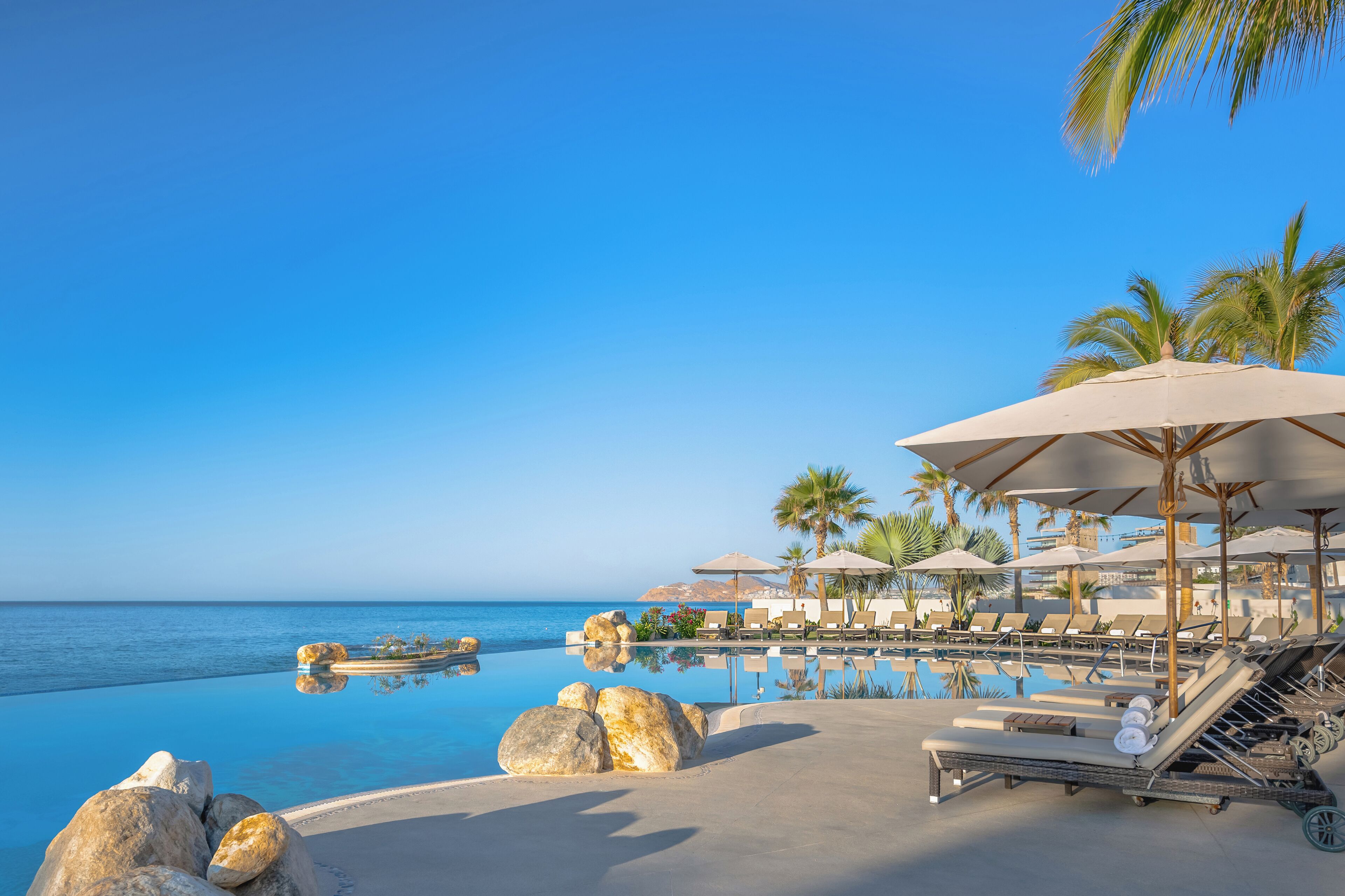 Ein Poolbereich mit Liegestühlen und Sonnenschirmen mit Blick auf das klare, blaue Meer.