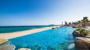 A clear blue pool adjacent to a sandy beach with a view of the ocean and distant mountains. - Villa La Valencia Beach Resort & Spa Los Cabos (San José del Cabo)