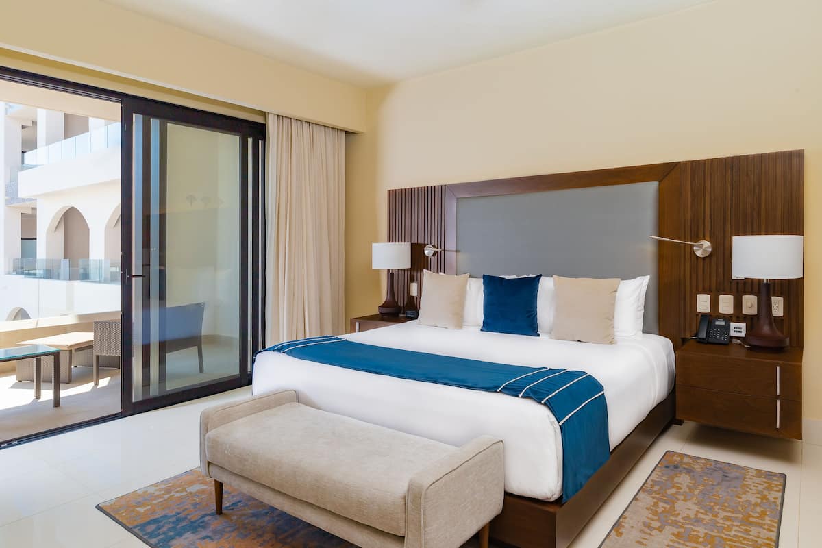 Ein Hotelzimmer mit einem großen Bett, einem Schreibtisch, einem Stuhl, einer Couch, einem kleinen Tisch und einem Fenster mit Vorhängen.
