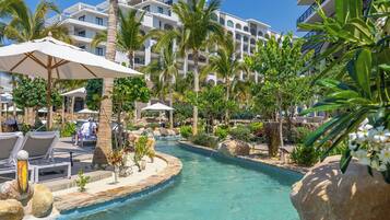 A resort pool area with lounge chairs, umbrellas, palm trees, and a clear blue pool.
