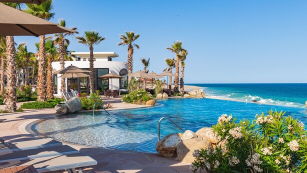 A pool area with lounge chairs, palm trees, and a view of the ocean. - Villa La Valencia Beach Resort & Spa Los Cabos (San José del Cabo)