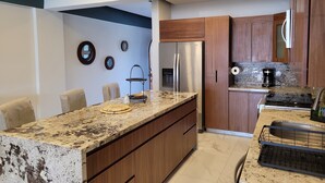 Eine moderne Küche mit einer Granit Arbeitsplatte, Holzschränken, einem Edelstahlkühlschrank und einer Kaffeemaschine.