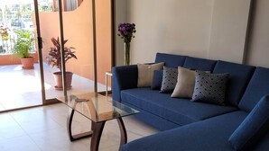 Ein modernes Wohnzimmer mit einem blauen Sofa, einem Glastisch und Topfpflanzen.