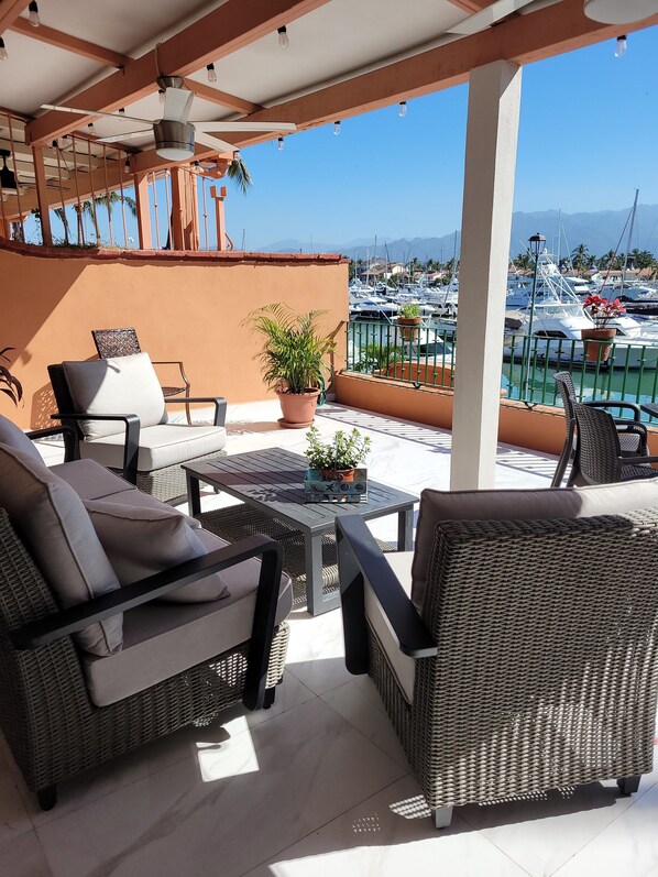 A covered outdoor seating area with wicker furniture and a view of a marina with boats.
