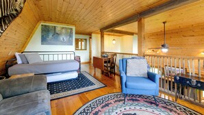 A cozy cabin interior with a loft bed, a sofa, a chair, and a dining area. - Sip, Soak & Unwind: Waynesville Cabin w/ Hot Tub (Waynesville)