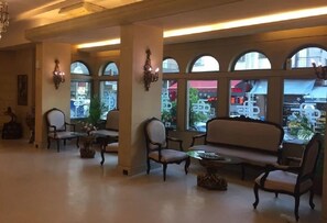 Un hall d’entrée avec un canapé, des fauteuils et une table. De grandes fenêtres à arc surmontent cet espace.