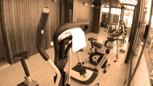 A gym with stationary bikes and elliptical machines, wooden walls, and glass doors leading to a bright area. - Royal Garden Hotel Beirut (Beirut)