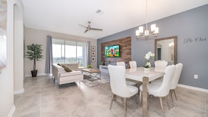 A modern dining area with a white table and chairs, a ceiling fan, and a large TV on the wall.