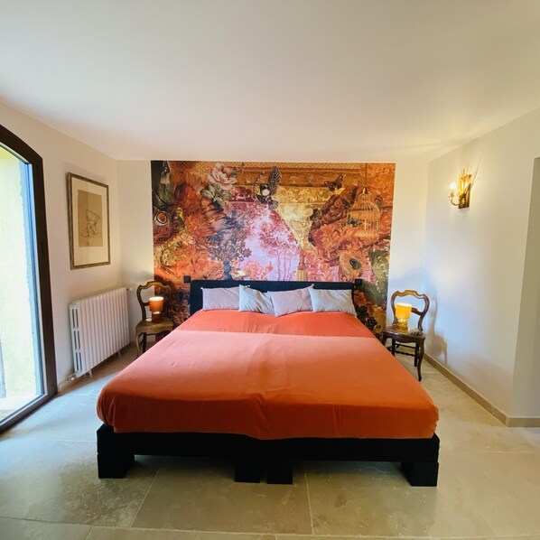A bedroom with a large bed, a radiator, a framed picture on the wall, and a window.