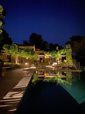 A nighttime view of a pool area with lounge chairs and a clear pool reflecting the surroundings.