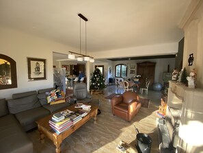 A spacious living room with a fireplace, a dining area, and a kitchen in the background.