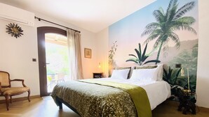 Un dormitorio con cama, una silla, una mesita de noche y un cuadro de una palmera.