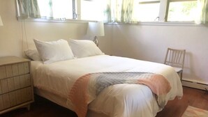 Une chambre à coucher avec un lit, une table de chevet, une chaise et une fenêtre avec des rideaux.