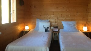 Une chambre chaleureuse en bois, aménagée comme un chalet, avec deux lits, chacun doté d’un oreiller et d’une table de chevet avec une lampe.