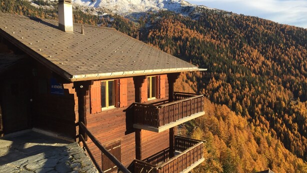 Un chalet en bois doté d’un balcon donnant sur une chaîne de montagnes boisées.