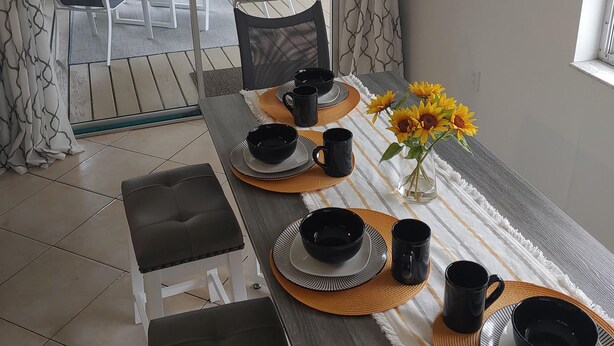 A dining area with a table set for four, featuring black and white plates, cups, and a vase with sunflowers. - Newly remodeled, all new furniture, beaches, shopping, restaurants, golf, tennis (Venice)