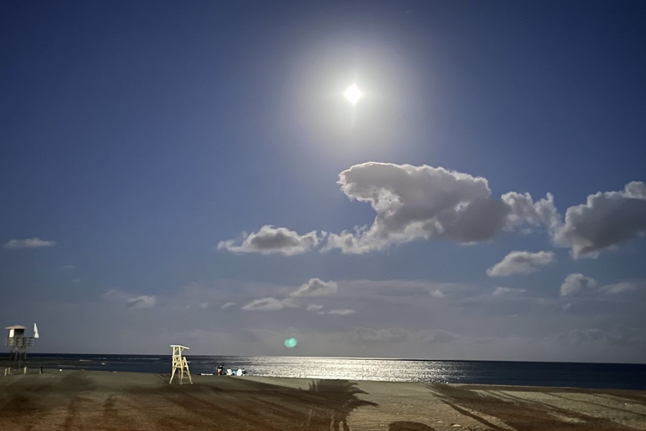 Een strand met een uitkijktoren voor de badmeester, heldere lucht en een kalme zee.