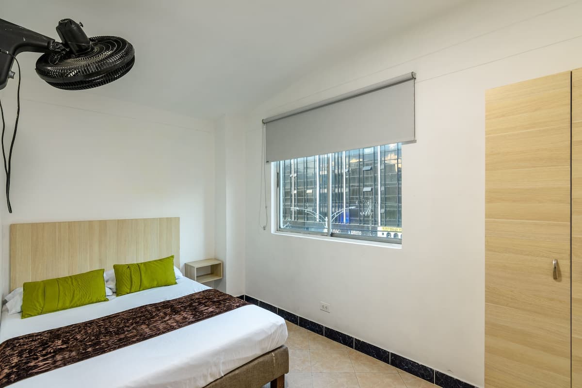 Una camera d'albergo con un letto, una finestra vista, un armadio in legno e una ventola a soffitto.