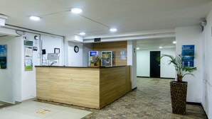 A reception desk with a wooden finish, a potted plant, and a tiled floor with directional markers. - Hotel Med Colombia (Medellín)