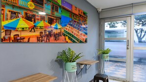 A colorful mural of a street scene, a wooden bench, two potted plants, and a view through a glass door. - Hotel Med Colombia (Medellín)