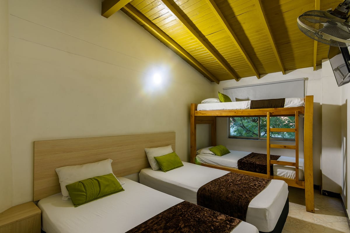Una stanza con due letti singoli e un letto a castello, travi in legno a vista al soffitto e una finestra che si affaccia sugli alberi.