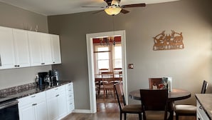 Una cucina con mobili bianchi, un'area pranzo con tavolo e sedie rotonde, e una ventola a soffitto.