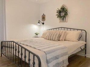 Une chambre à coucher avec un lit, une table de chevet, une horloge murale, une plante suspendue et une lampe sur pied.